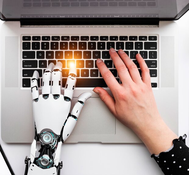 A human and robot hand are placed on a laptop keyboard